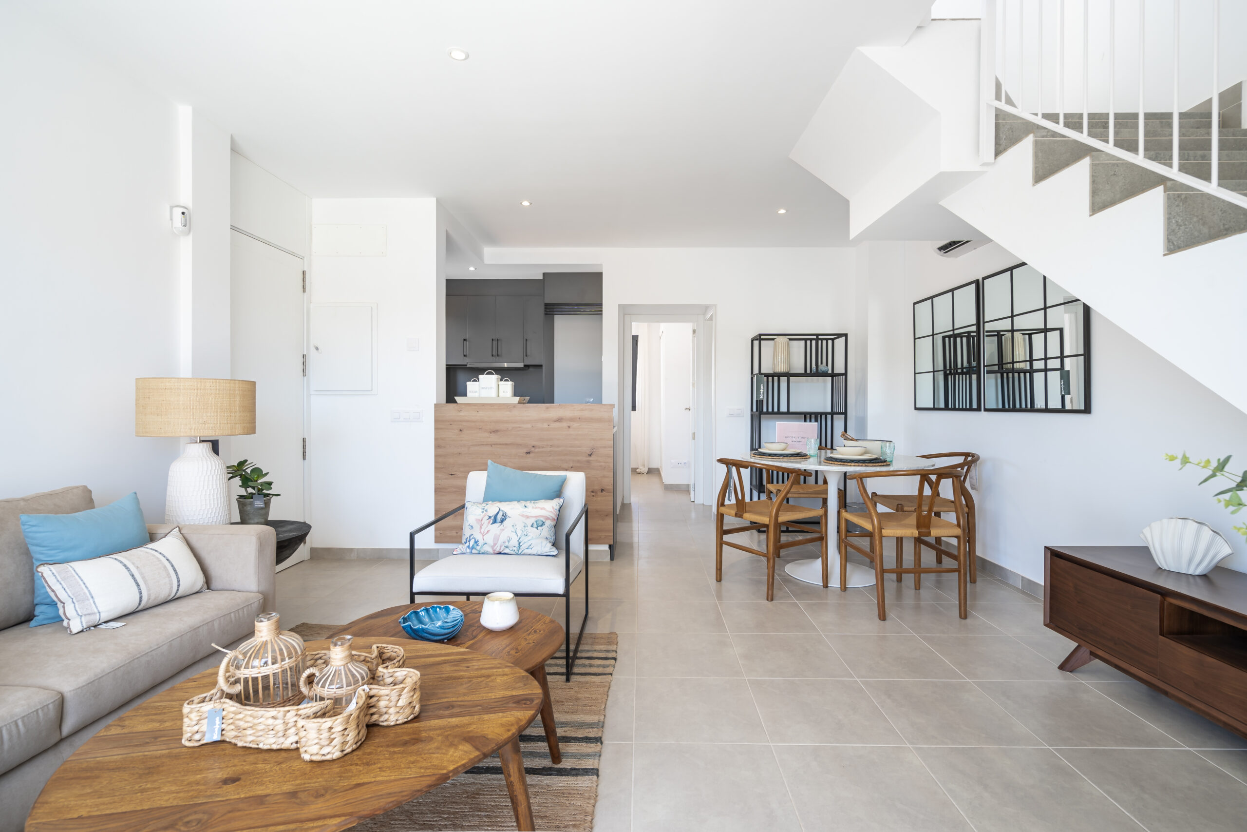 Helles, modern eingerichtetes Wohnzimmer mit offener Küche, Essbereich und gemütlicher Sitzecke, kombiniert mit natürlichen Holzelementen und neutralen Farbtönen.