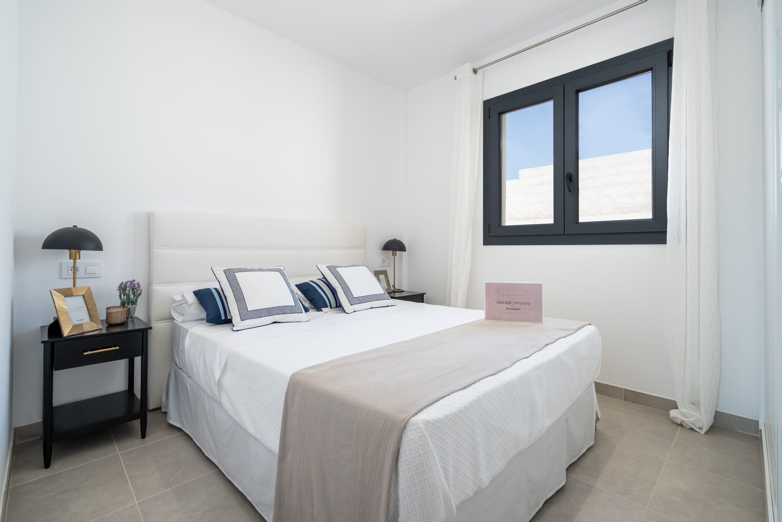Helles Schlafzimmer mit Doppelbett, neutraler Bettwäsche, zwei Nachttischen und großem Fenster mit Blick nach draußen.